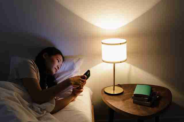 woman in bed looking at her smartphone causing smartphone stress