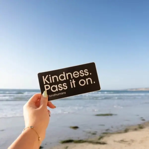 woman holding a sign saying kindness pass it on