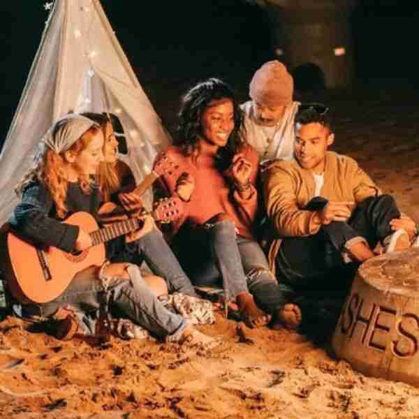 group of friends sitting in the sand in the glow of a fire showing the importance of a tribe