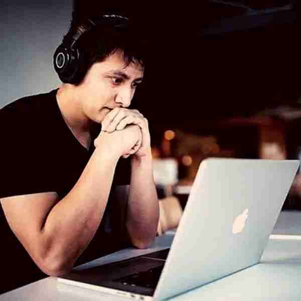 man looking at a laptop with headphones on showing the benefits of self-coaching