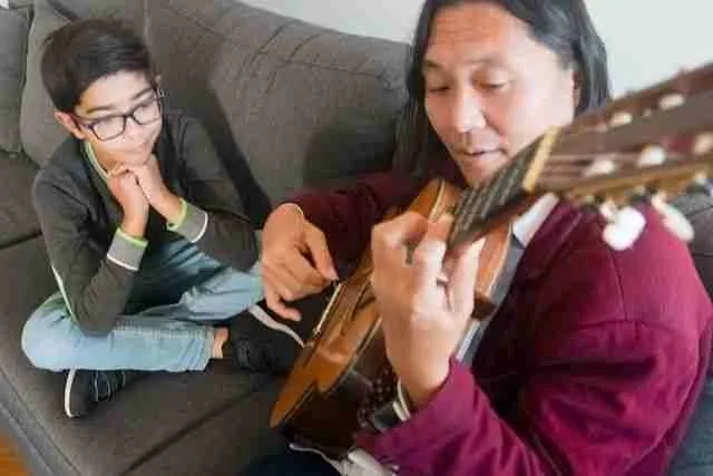 man playing guitar for son as music for self-care