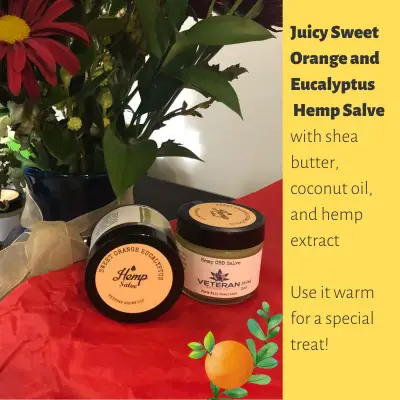 2 Jars of Sweet Orange and Eucalyptus Hemp Salve next to woodland flowers