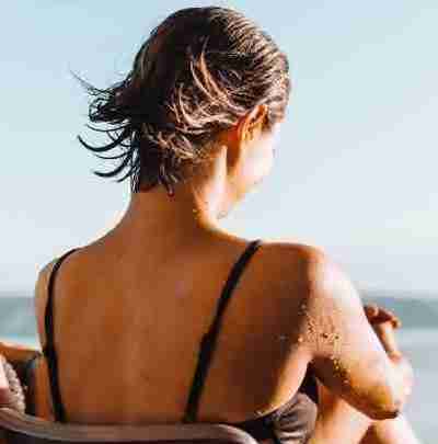 woman sitting on a beach in the sunshine looking at the water
